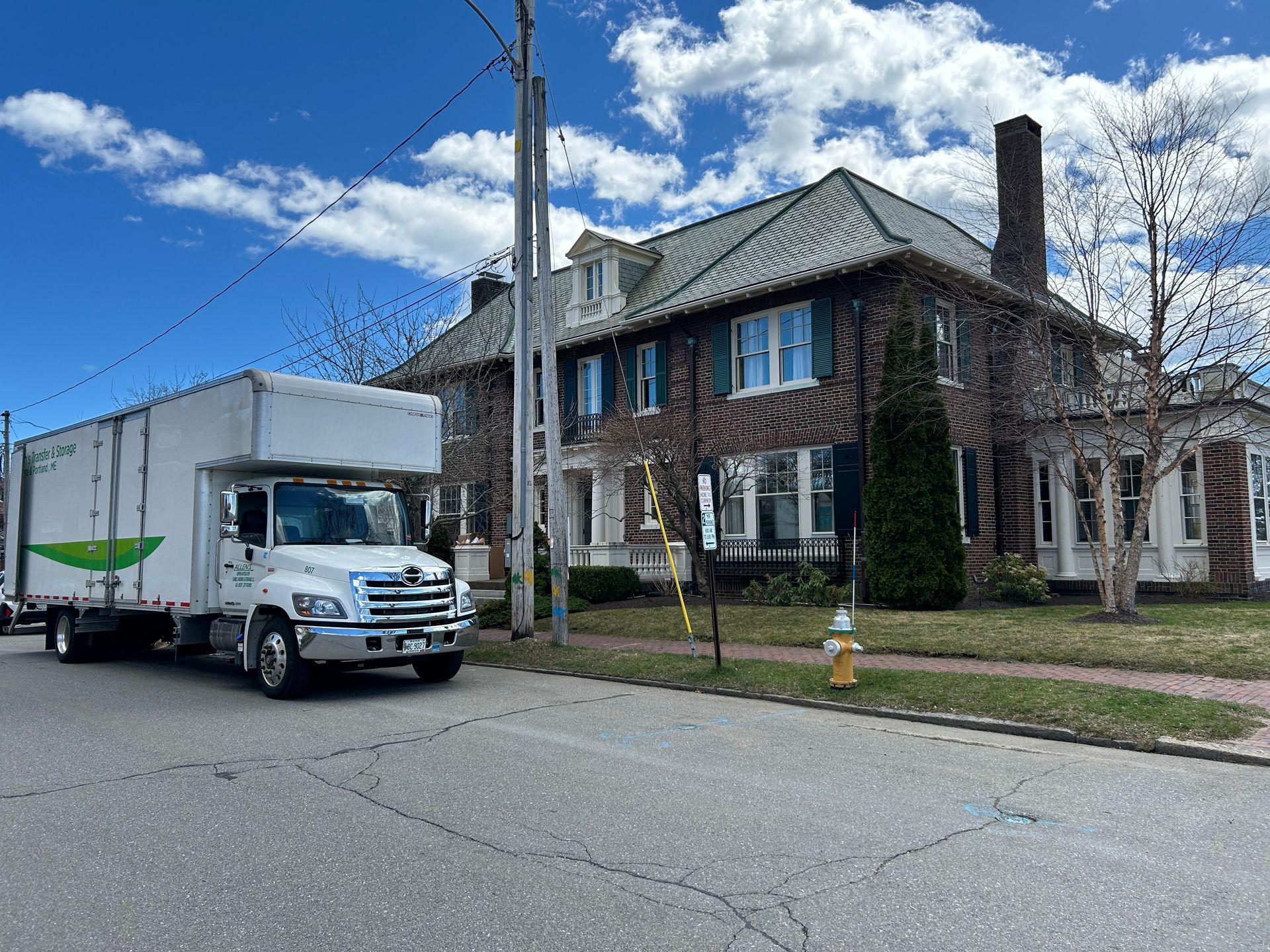 A white moving truck is parked in front of a large brick house.