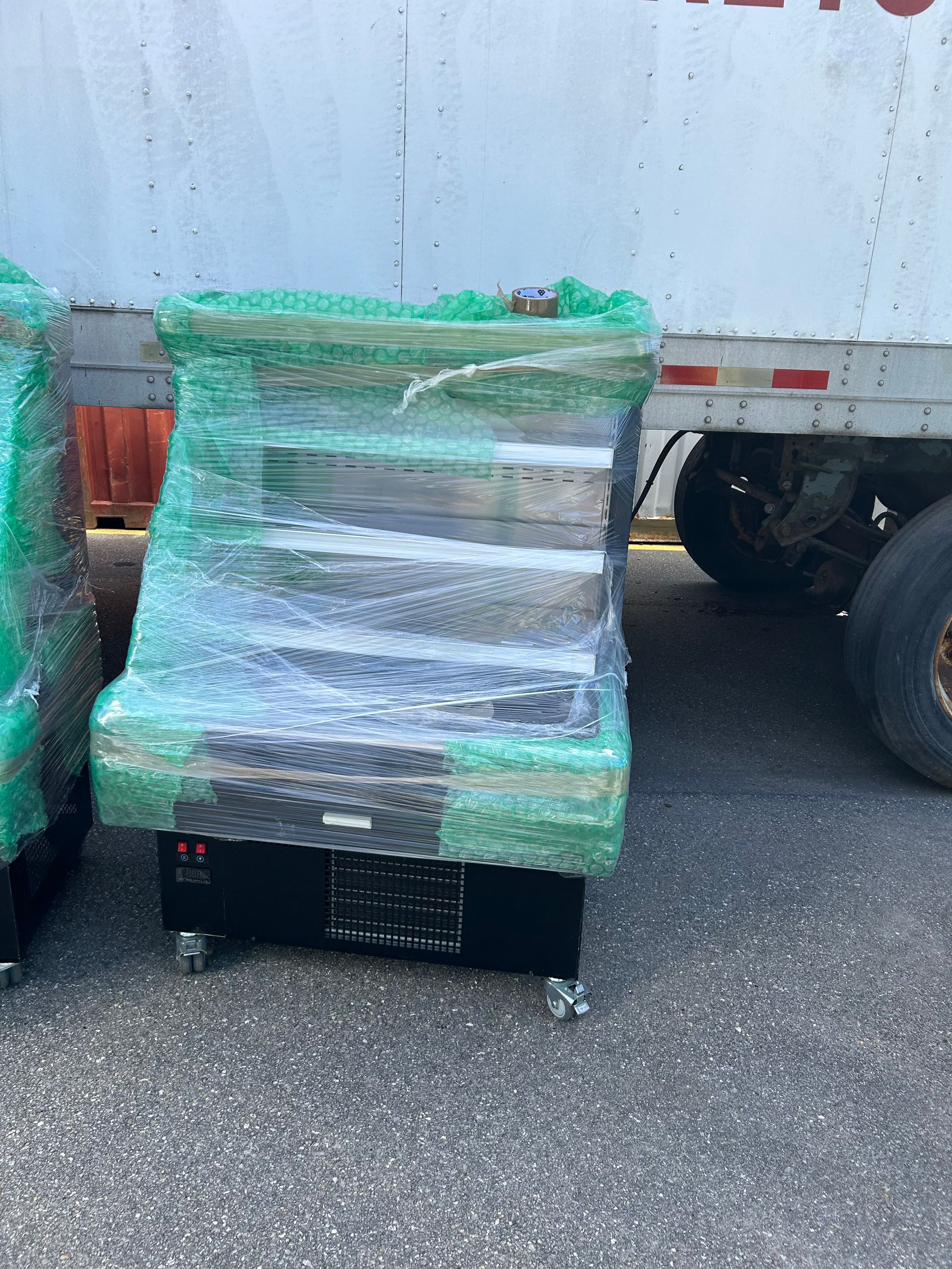 A white truck is parked next to a row of boxes wrapped in plastic.