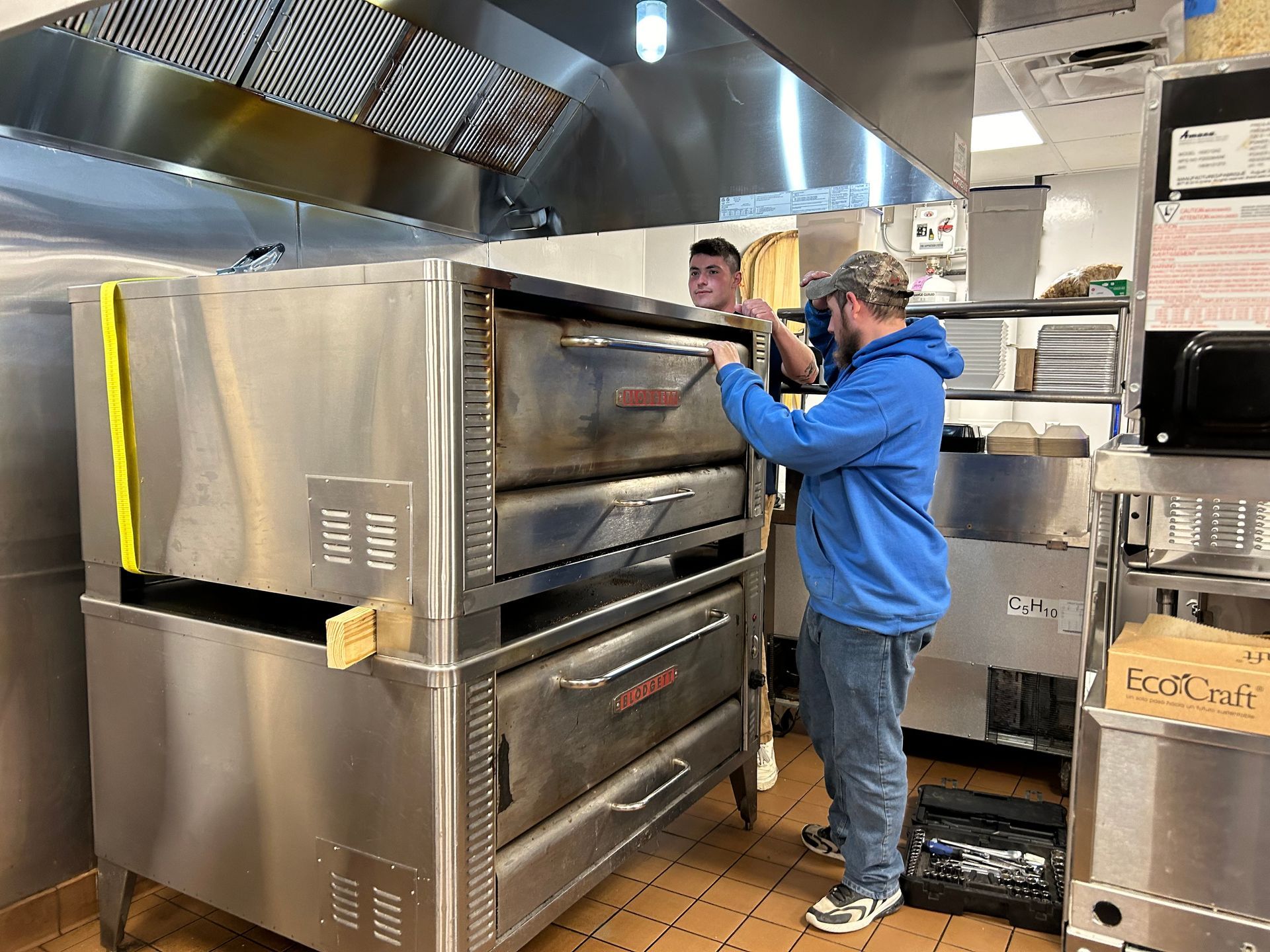 A man is working on a pizza oven in a restaurant kitchen.