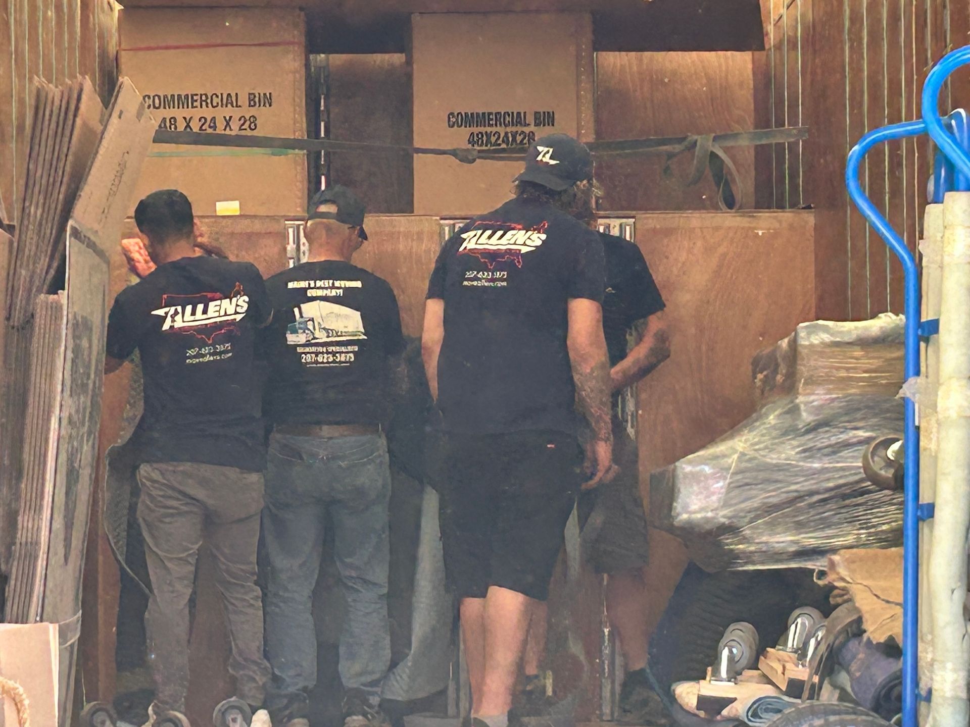 A group of men are standing in front of a truck filled with boxes.