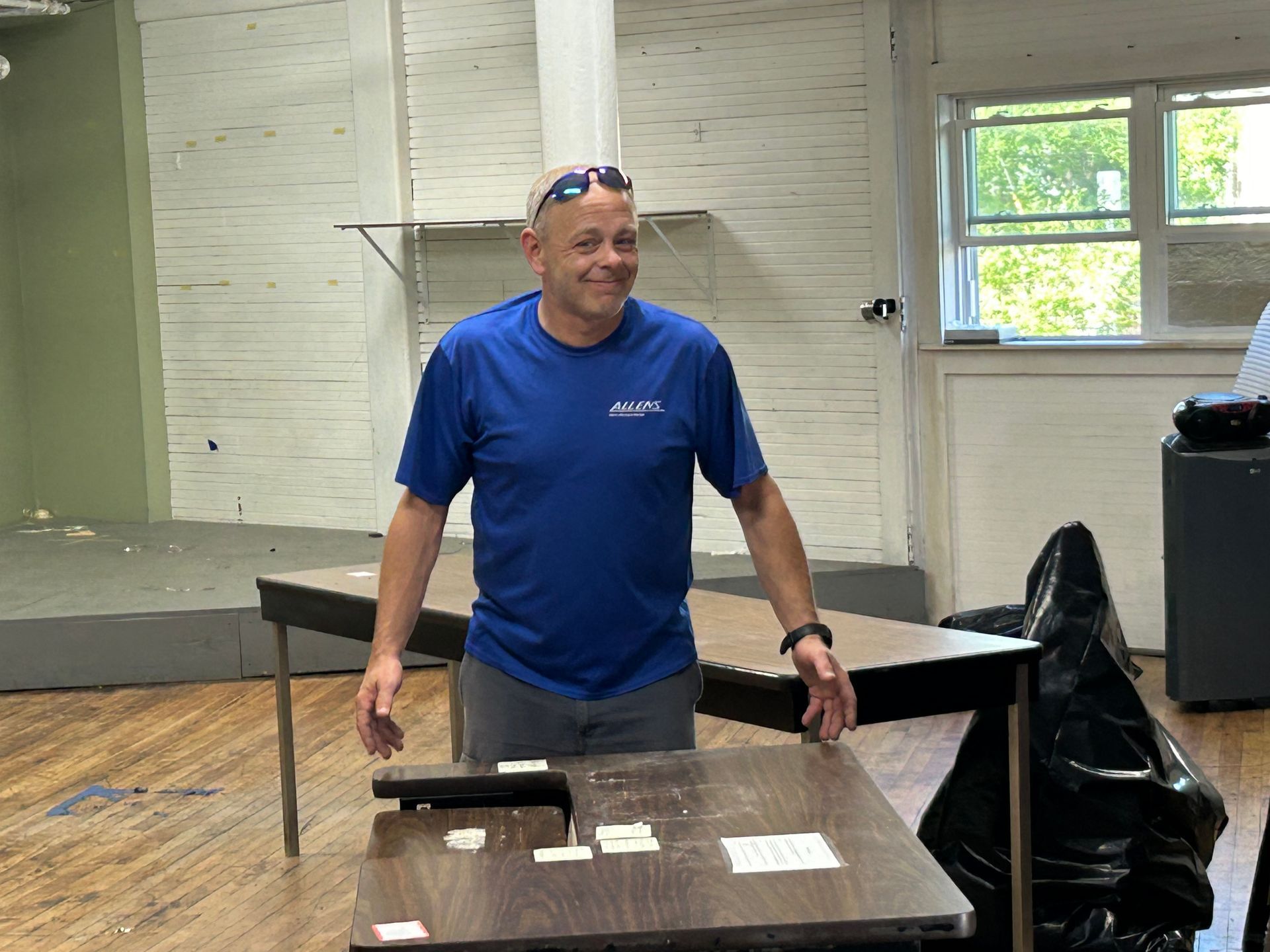 A man in a blue shirt is standing in front of a table.