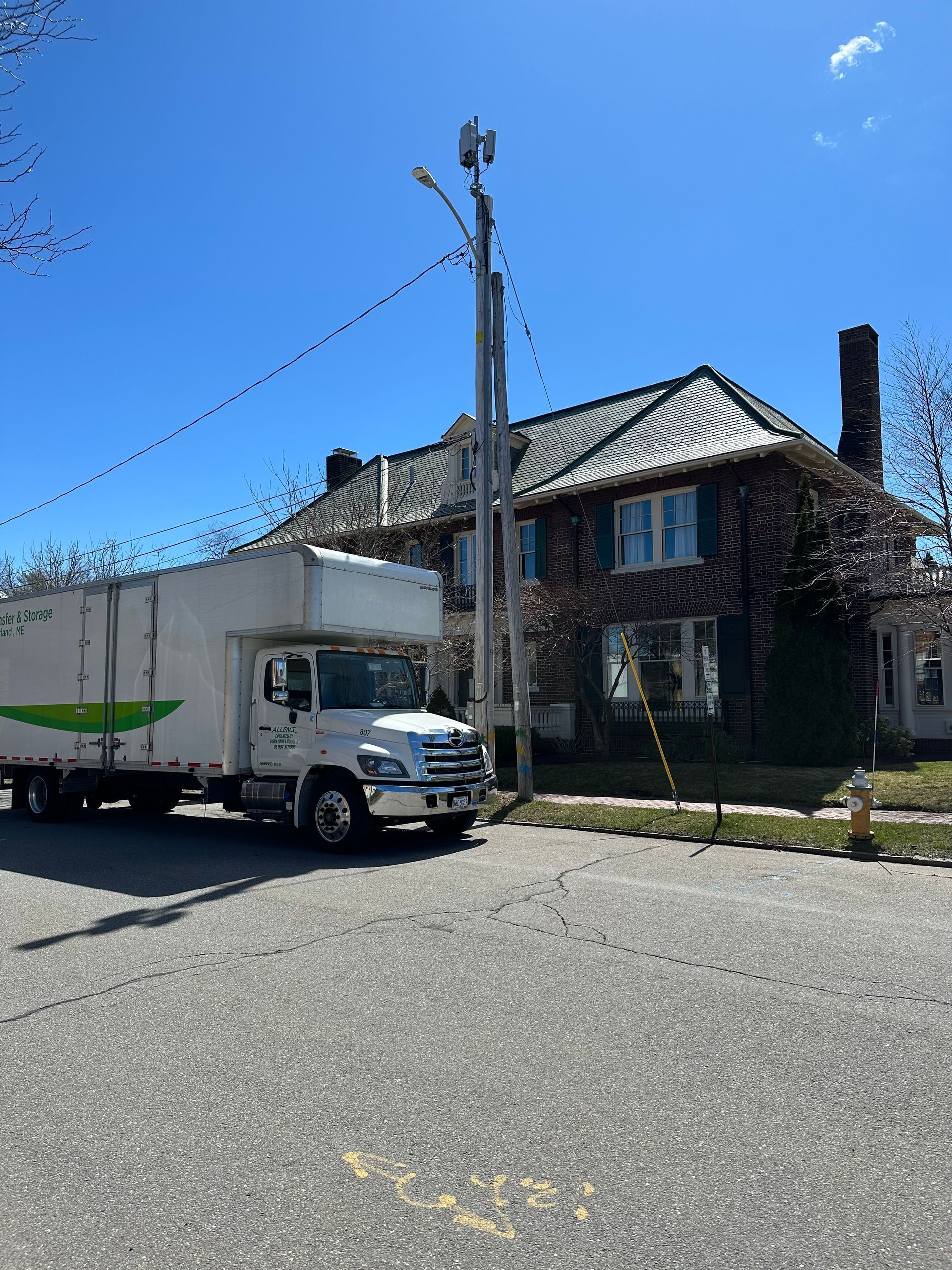 A white moving truck is parked on the side of the road in front of a brick house.