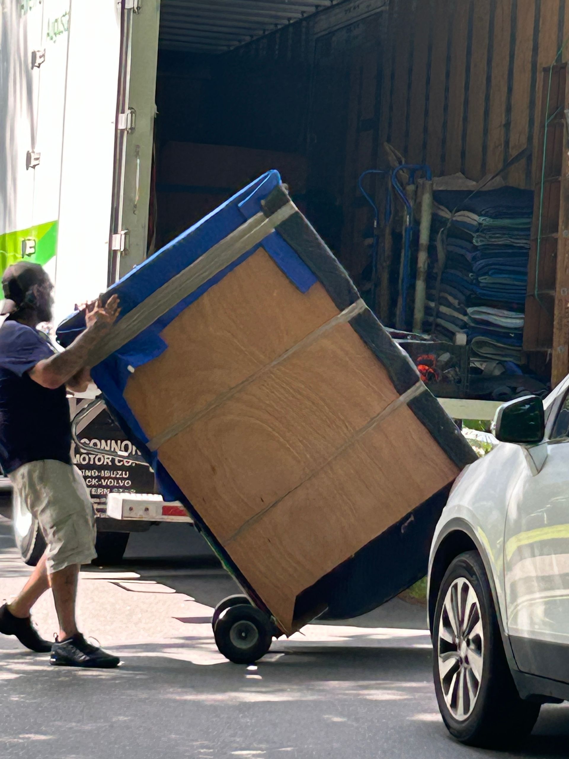 A man is pushing a large piece of furniture on a cart