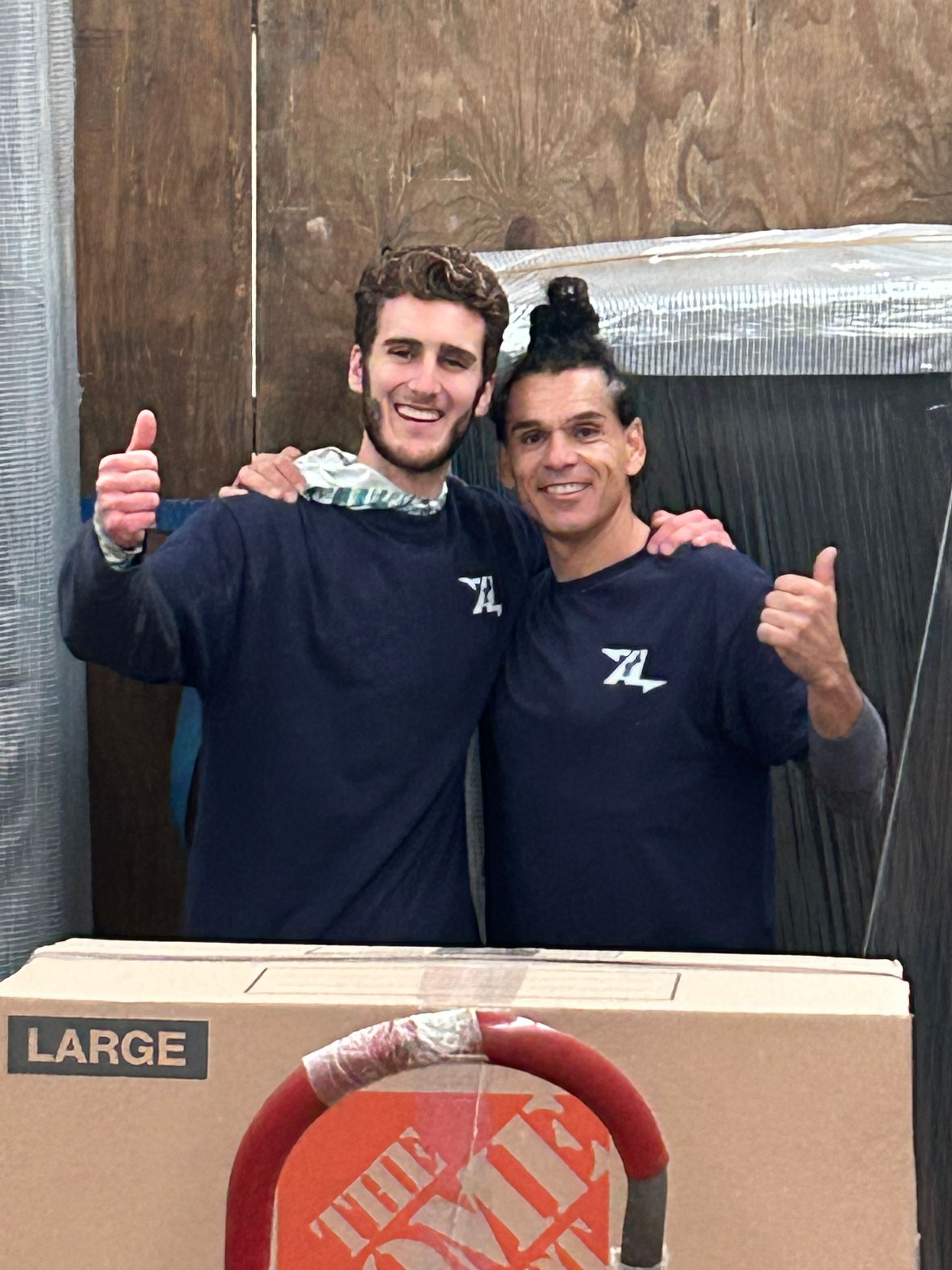 Two men giving a thumbs up in front of a large home depot box