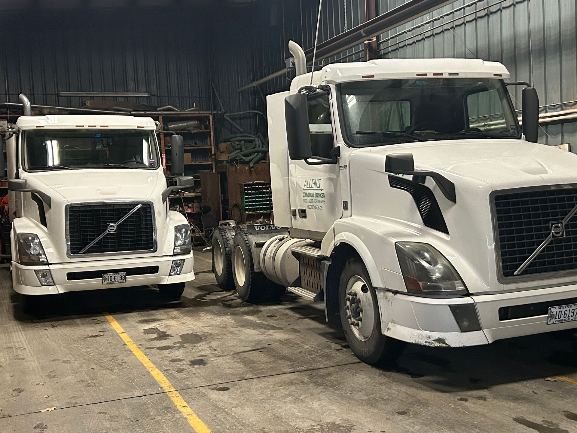 Two white semi trucks are parked next to each other in a garage.