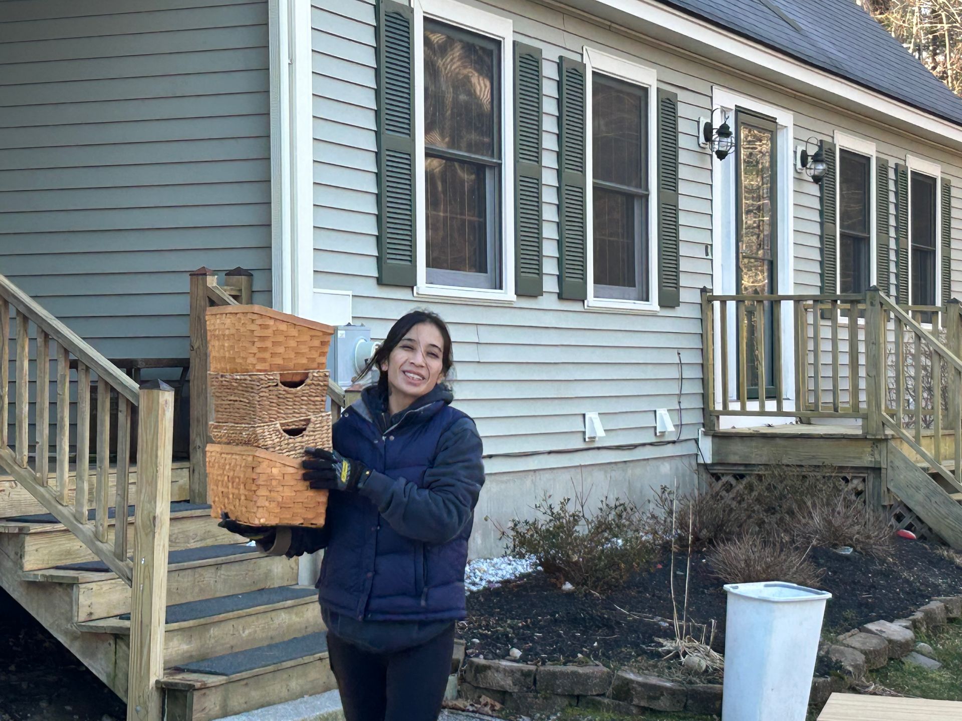 A woman is holding a wooden box in front of a house.