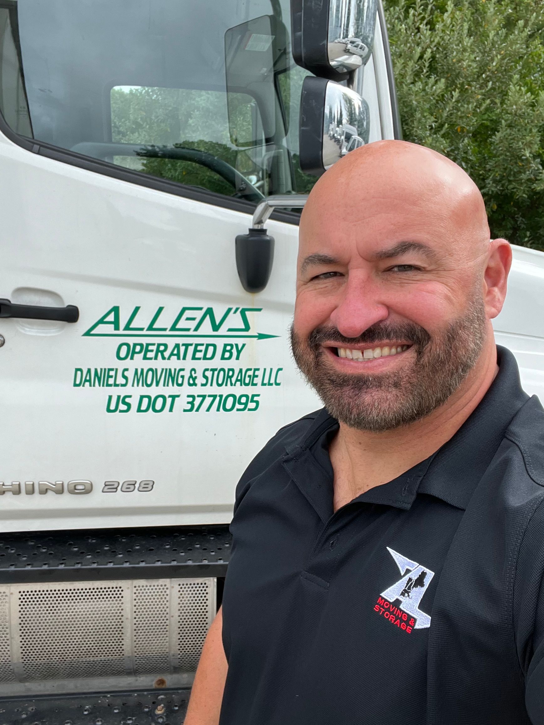 A bald man with a beard is smiling in front of a white truck.