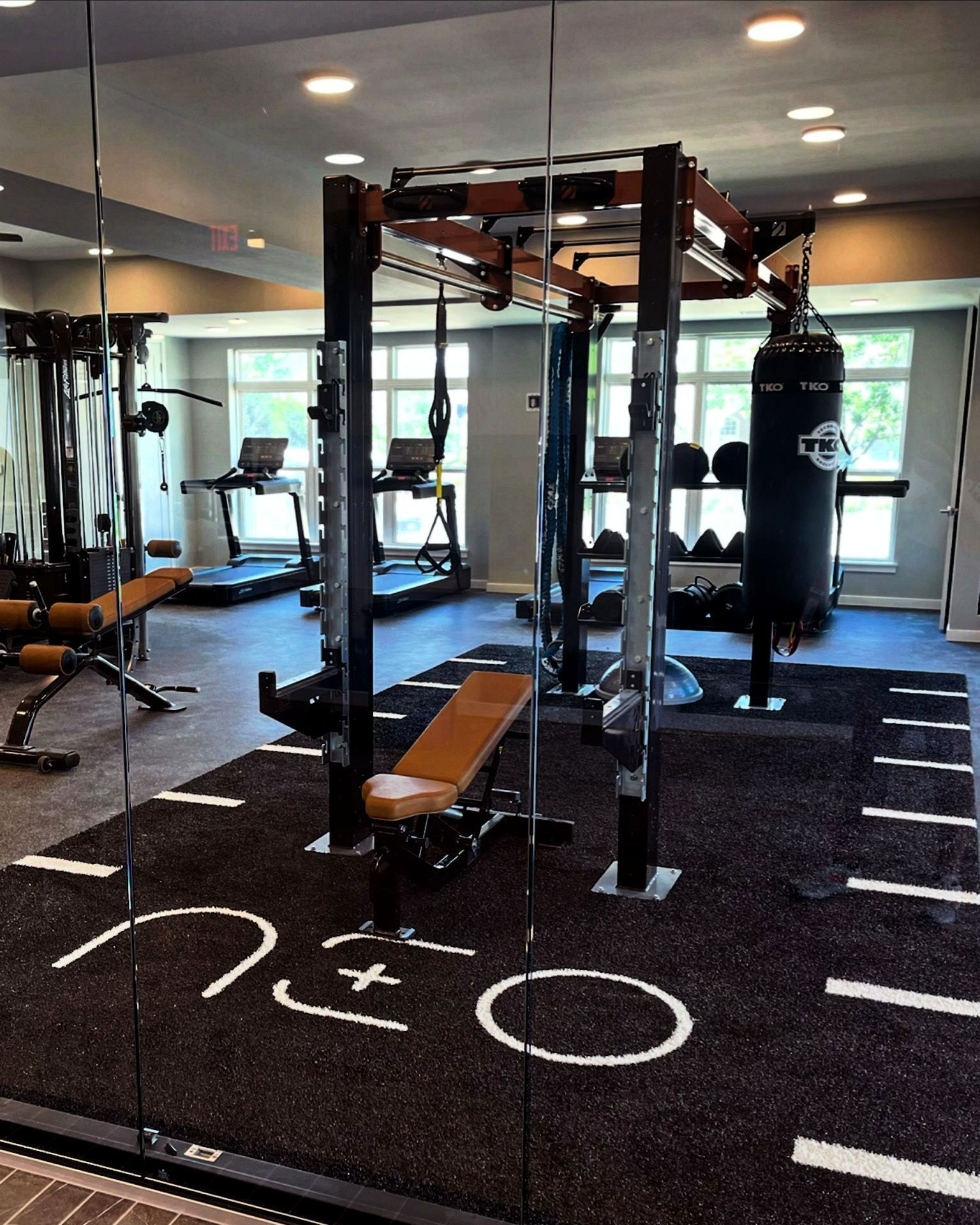 Modern gym interior with a power rack, bench, weights, and black rubber flooring with white markings
