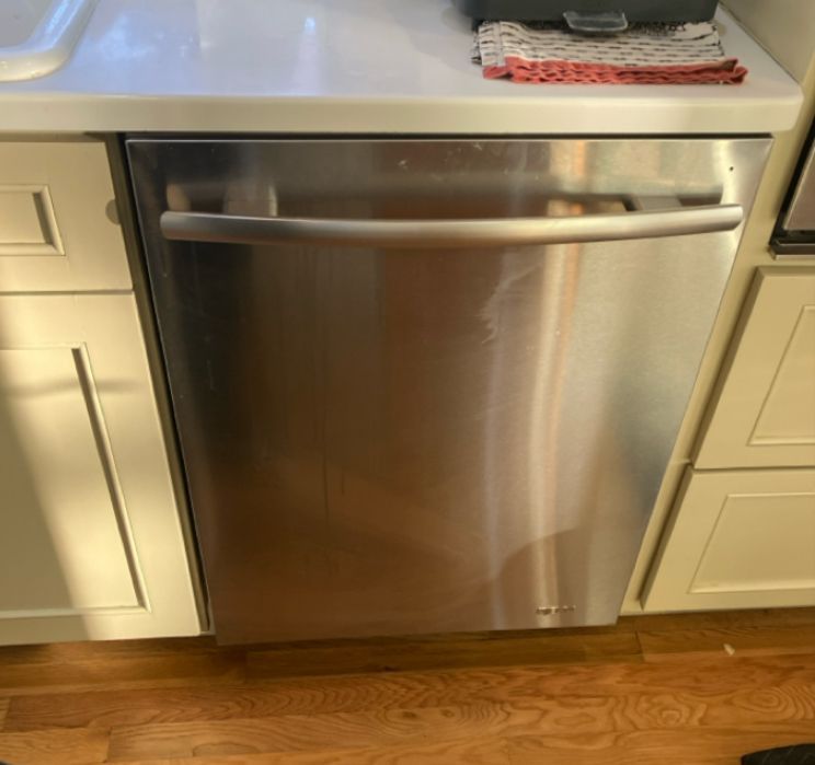 A stainless steel refrigerator is sitting on a wooden floor.