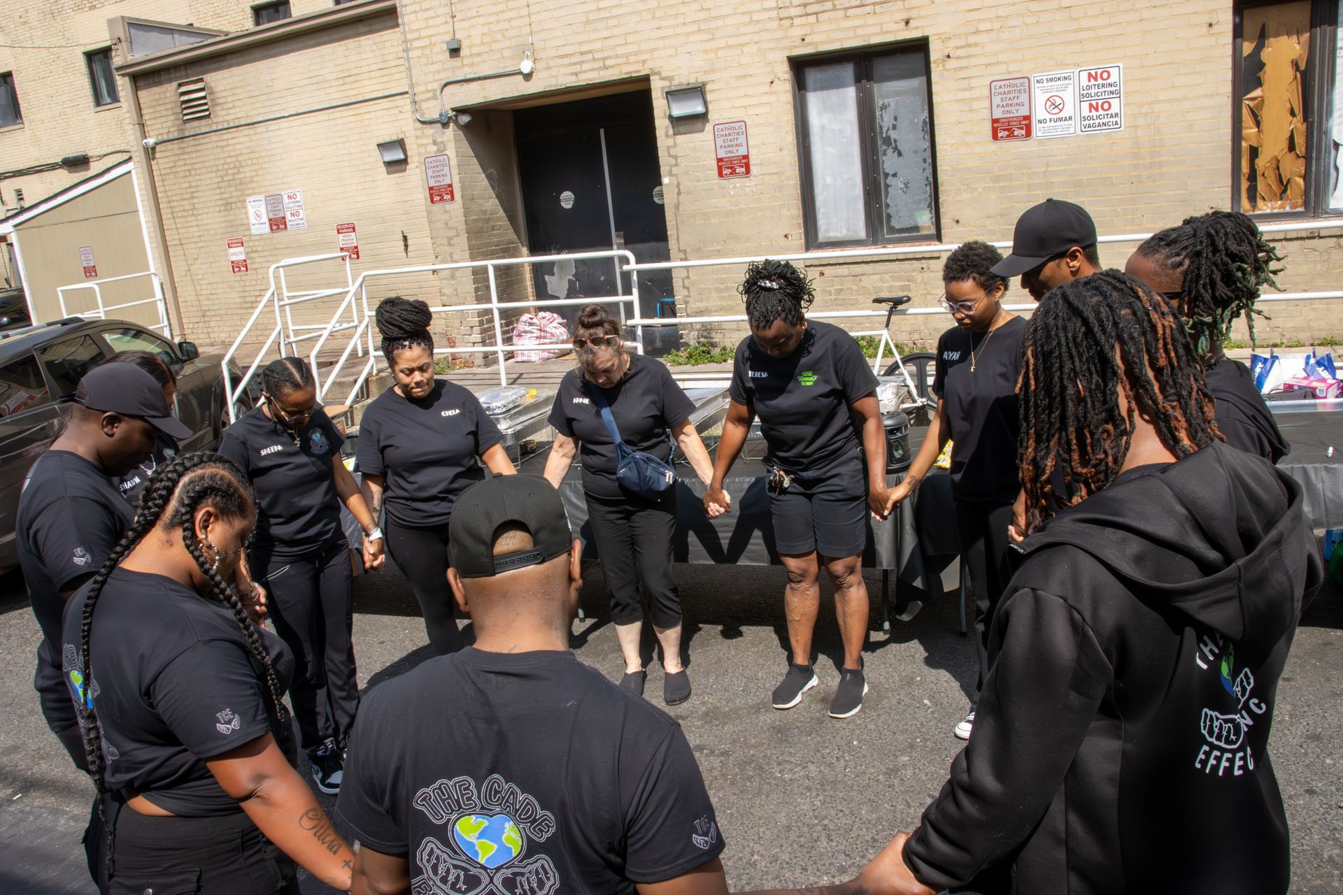 A group of people are standing in a circle holding hands in front of a building.