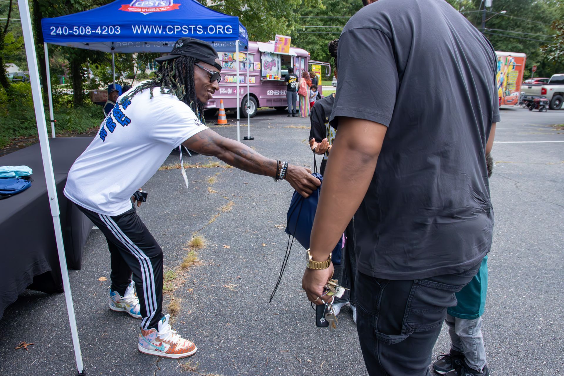A man in a white shirt is talking to another man in a parking lot.