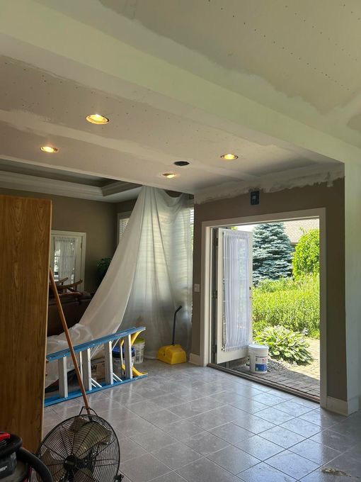 Room under construction; drywall dust shield, ladder, open doorway to a garden, recessed lighting.