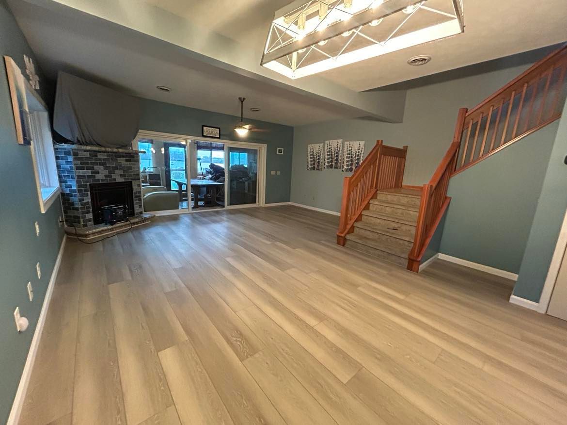 Spacious finished basement with wood floors, a fireplace, stairs, and glass doors.