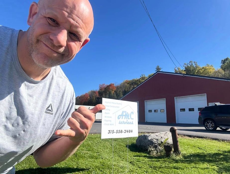Man pointing at a sign for ABC Auto with a red building behind him on a sunny day.