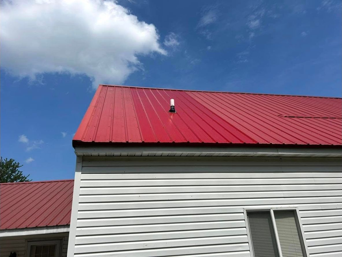 Red metal roof on a white house against a blue sky with white clouds.