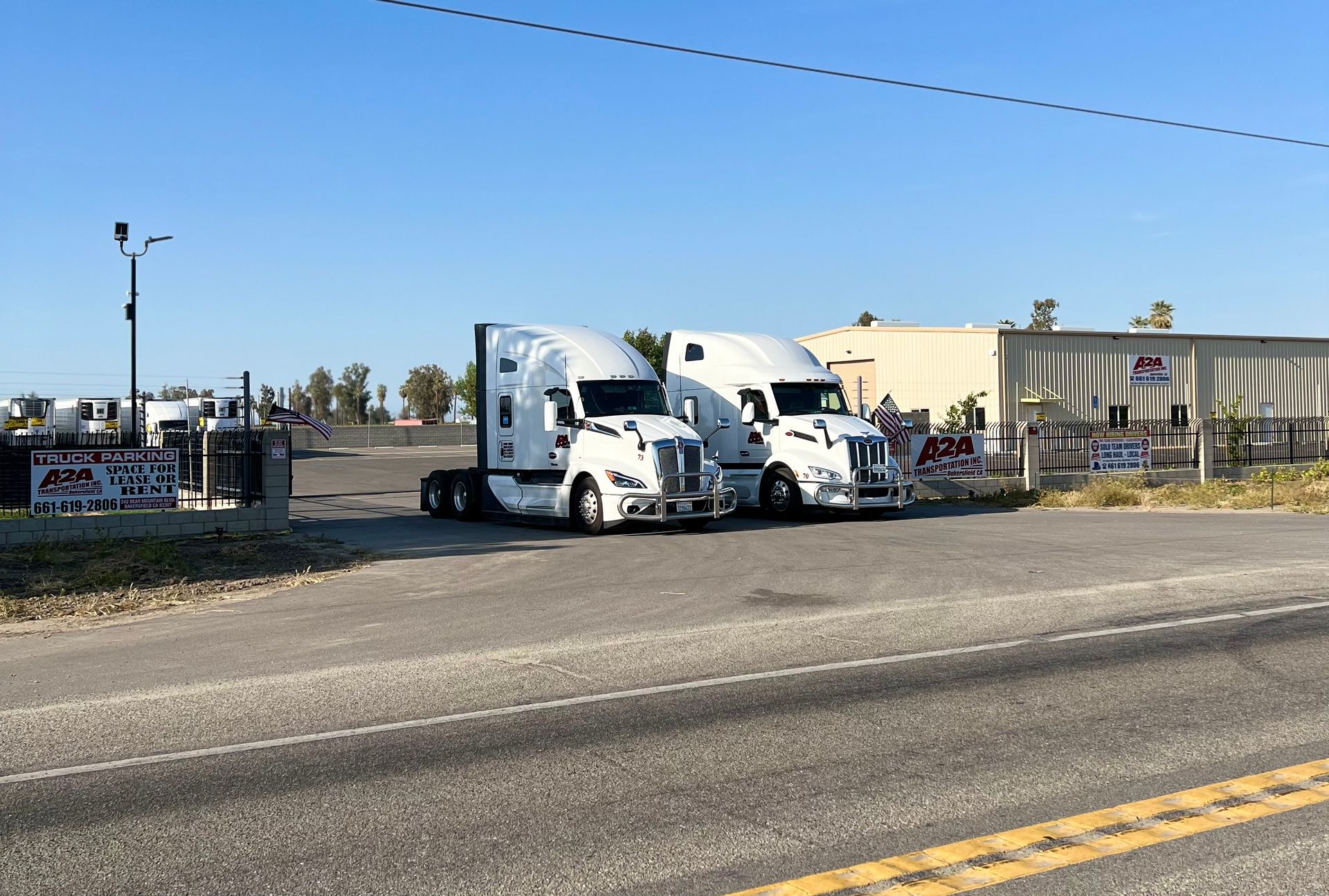 two semi-trucks are parked on the side of the road in front of the A2A Transportation Inc. shop.