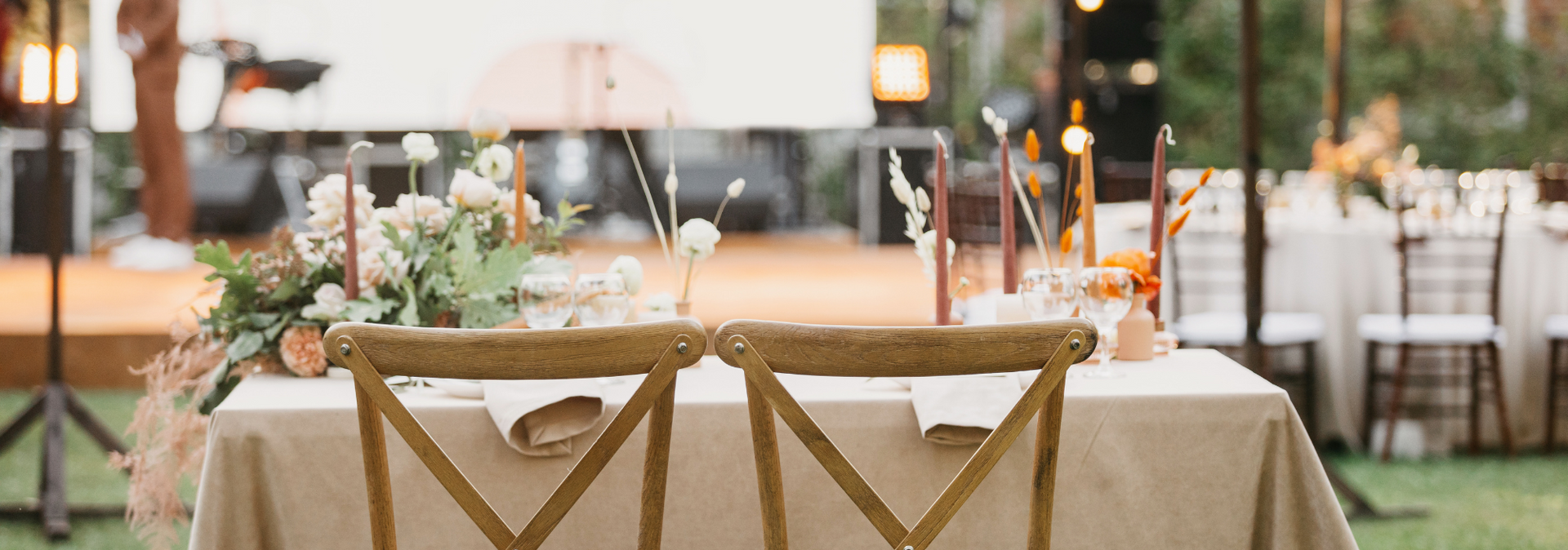 Decorated outdoor wedding reception table with white tablecloth, wooden chairs, and floral centerpieces
