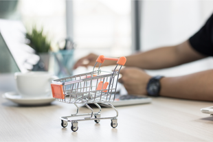 A shopping cart is sitting on a table next to a person using a laptop.