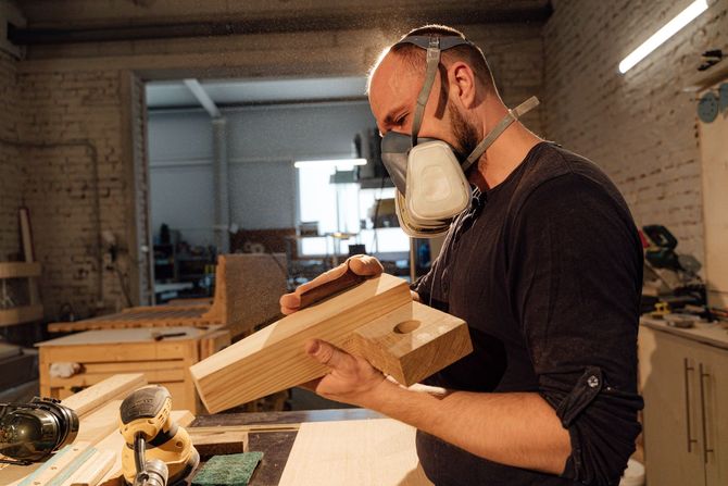 Man wearing a respirator sanding a wooden board in a workshop