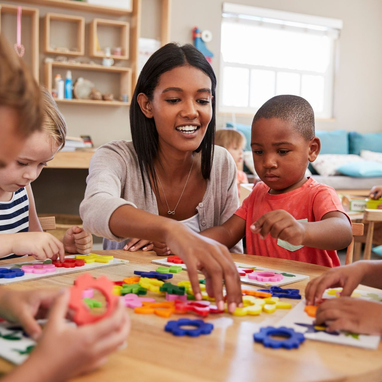 Preschool teacher helping diverse children with colorful toys during activity time at school.