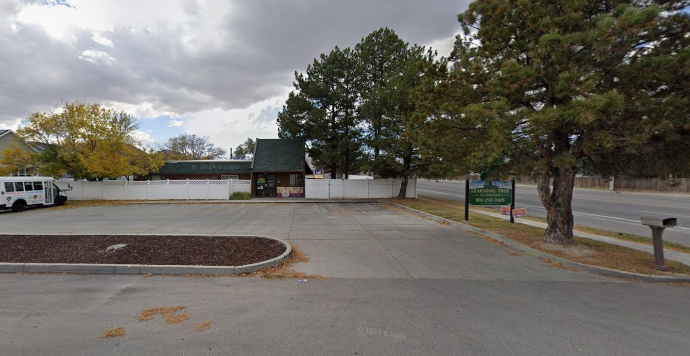 Building with a green roof and white fence, next to a road and trees on a cloudy day.