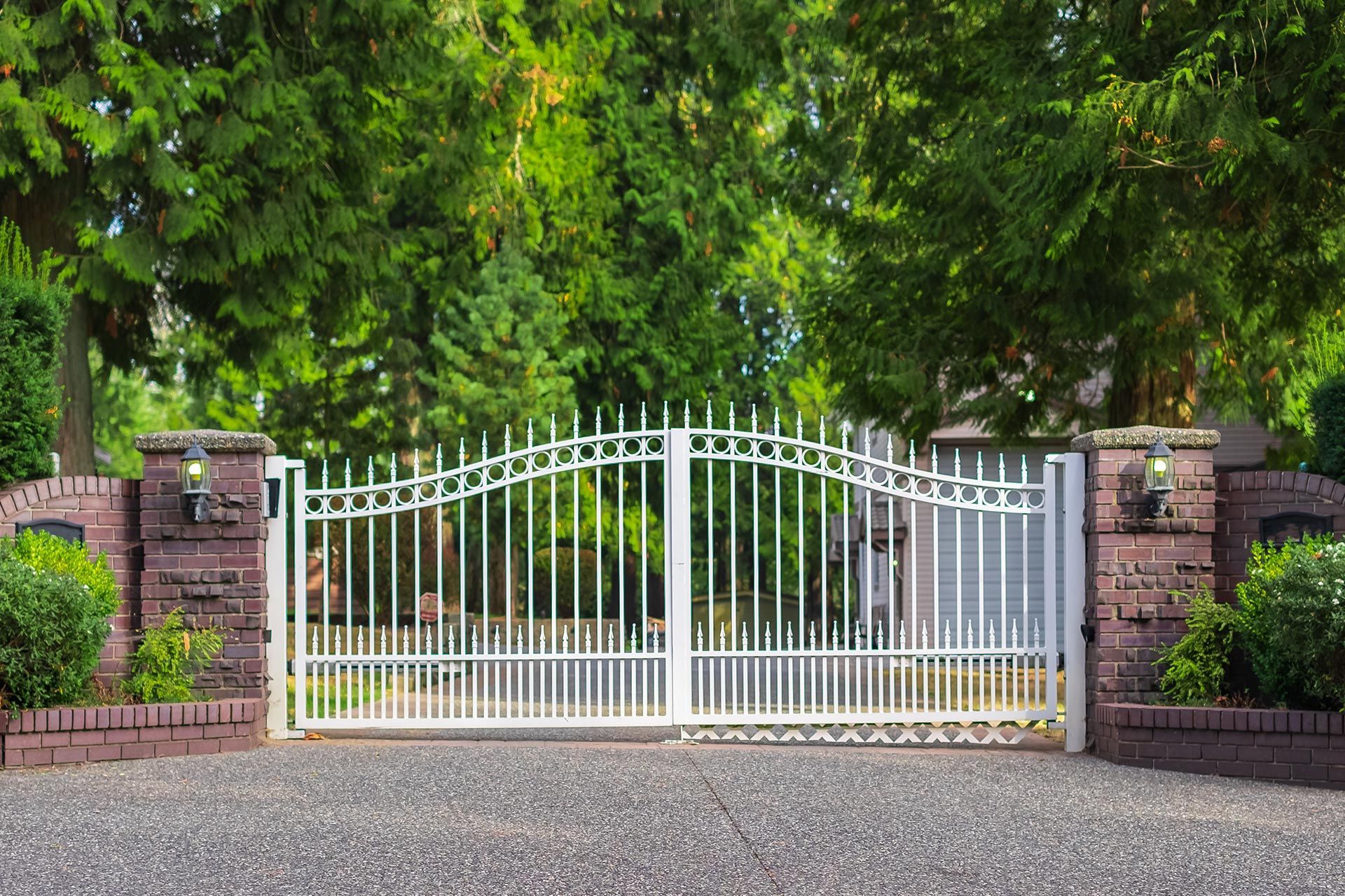 Elegant white gate with brick pillars and lights, leading to a private tree lined driveway.