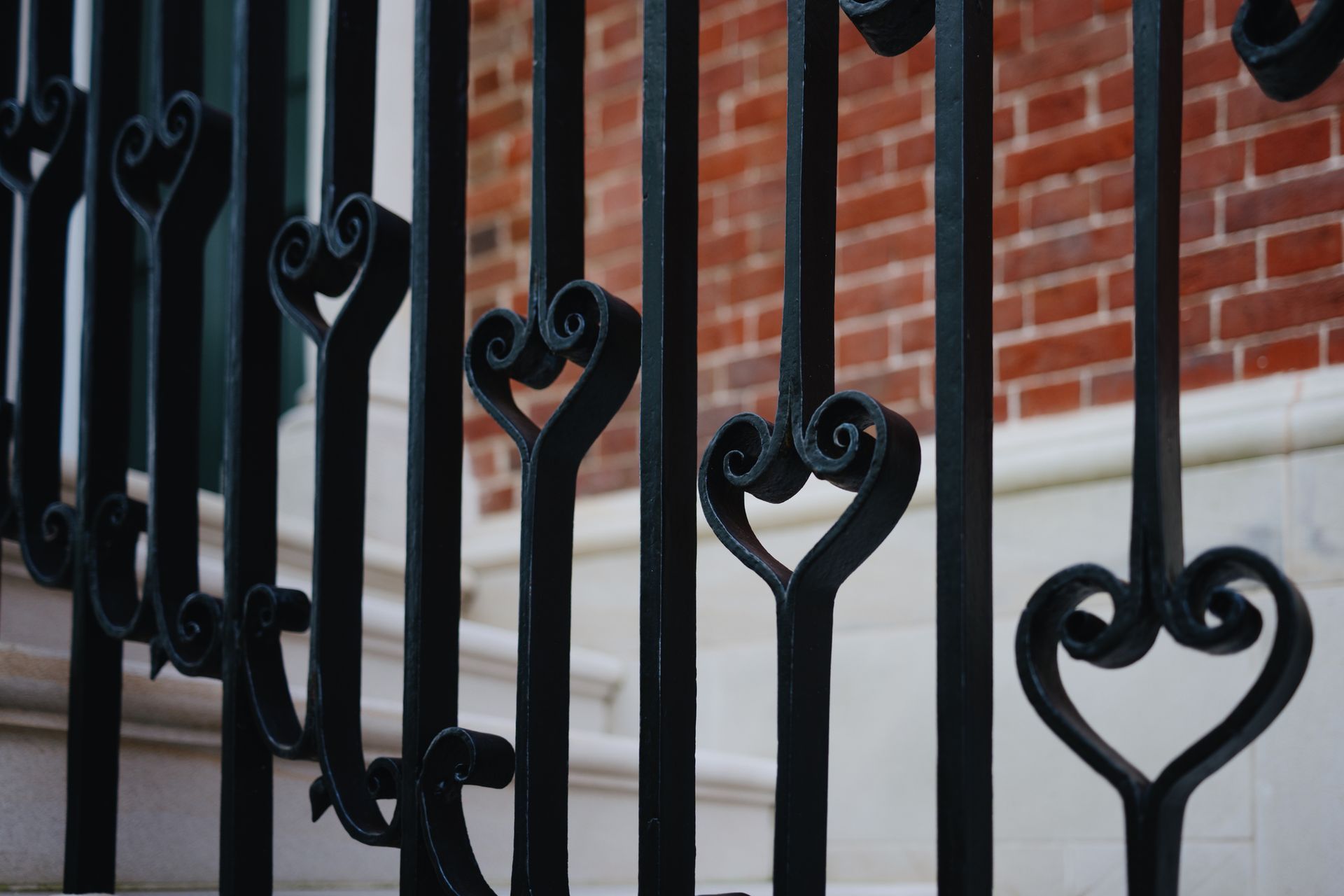 Close-up of ornate black iron fence with brick wall in background. Close-up of ornate black iron fence with brick wall in background.