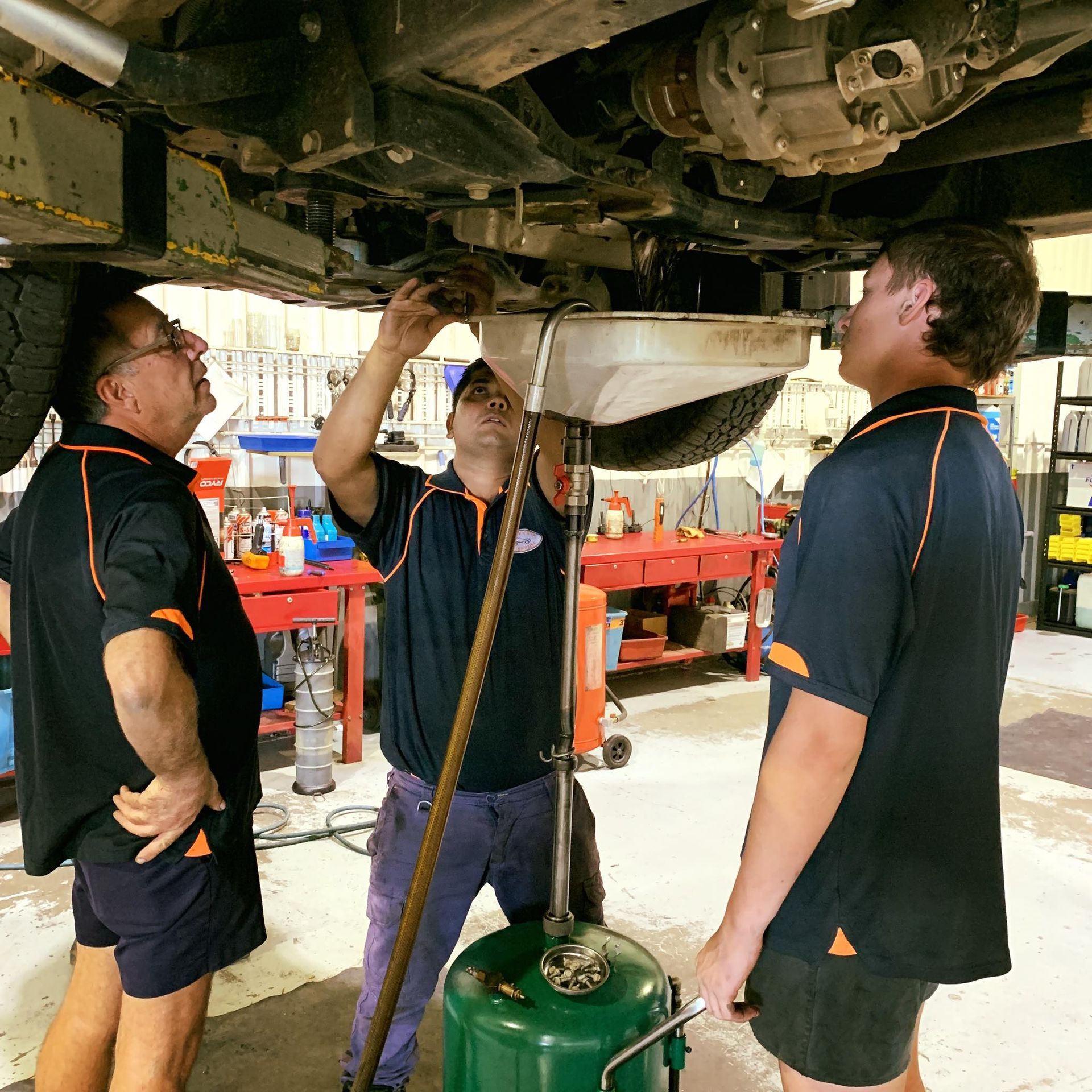 three mechanics working on a car. doing automotive repairs