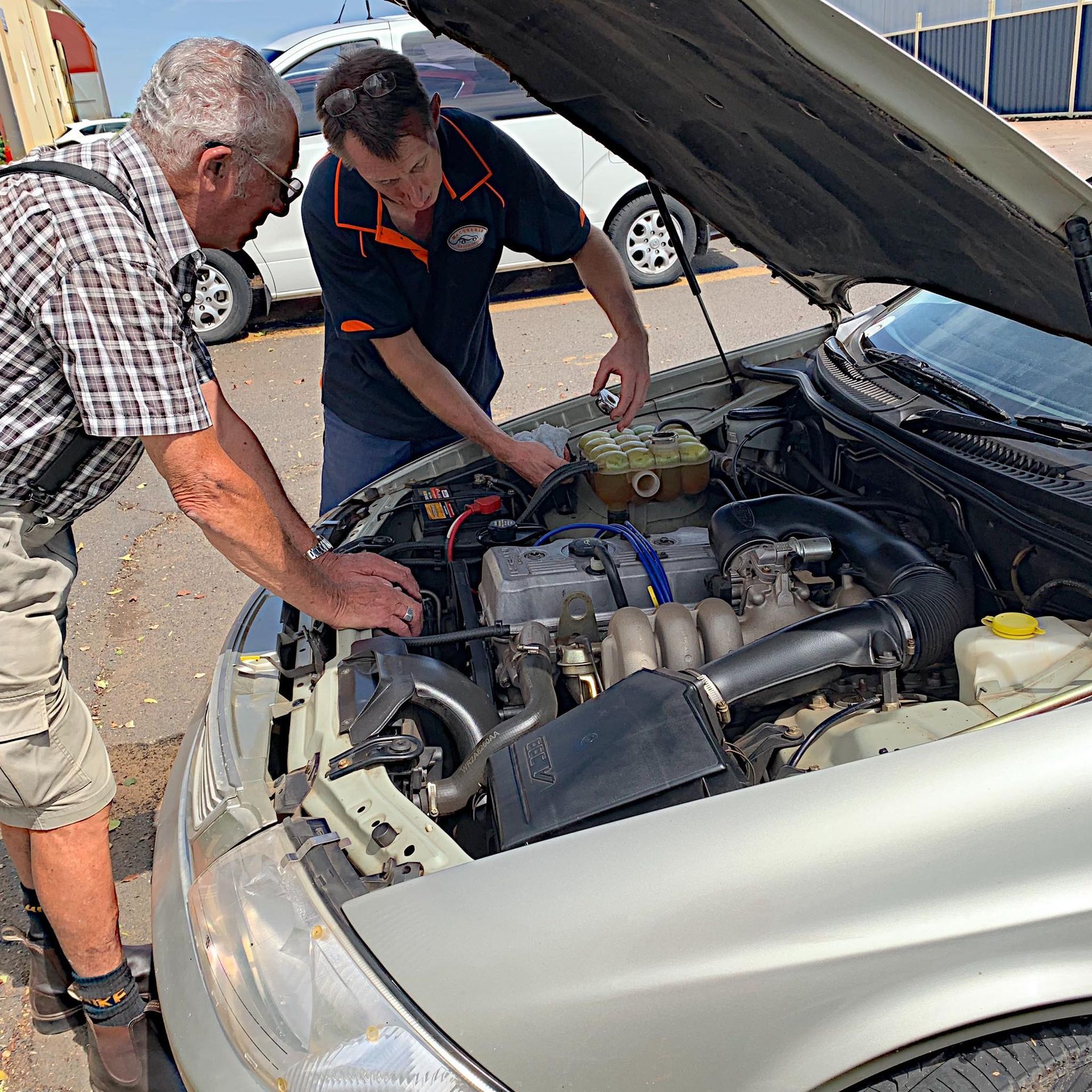 people standing over the open hood of a car and working on it.