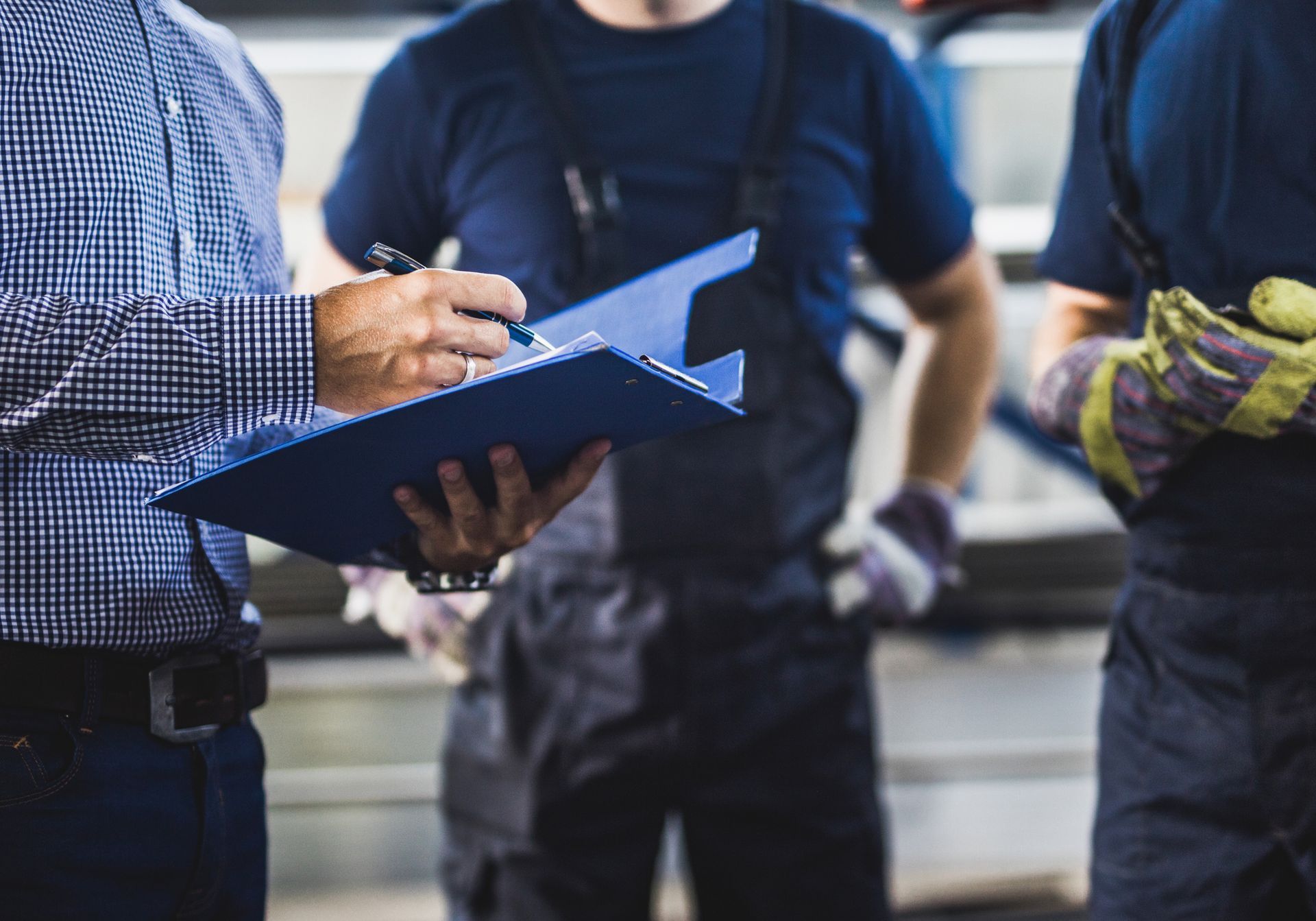 A man is holding a clipboard and writing on it while standing next to two other men.