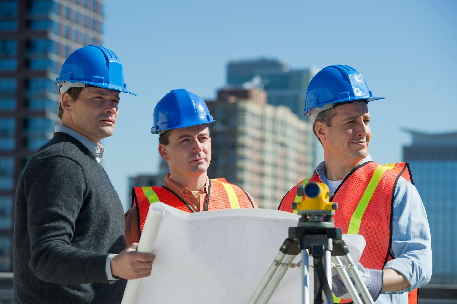 Three construction workers are standing next to each other looking at a blueprint.