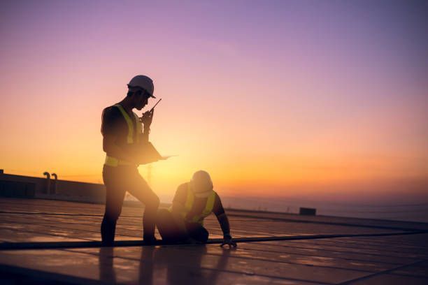 Two construction workers are working on a roof at sunset.