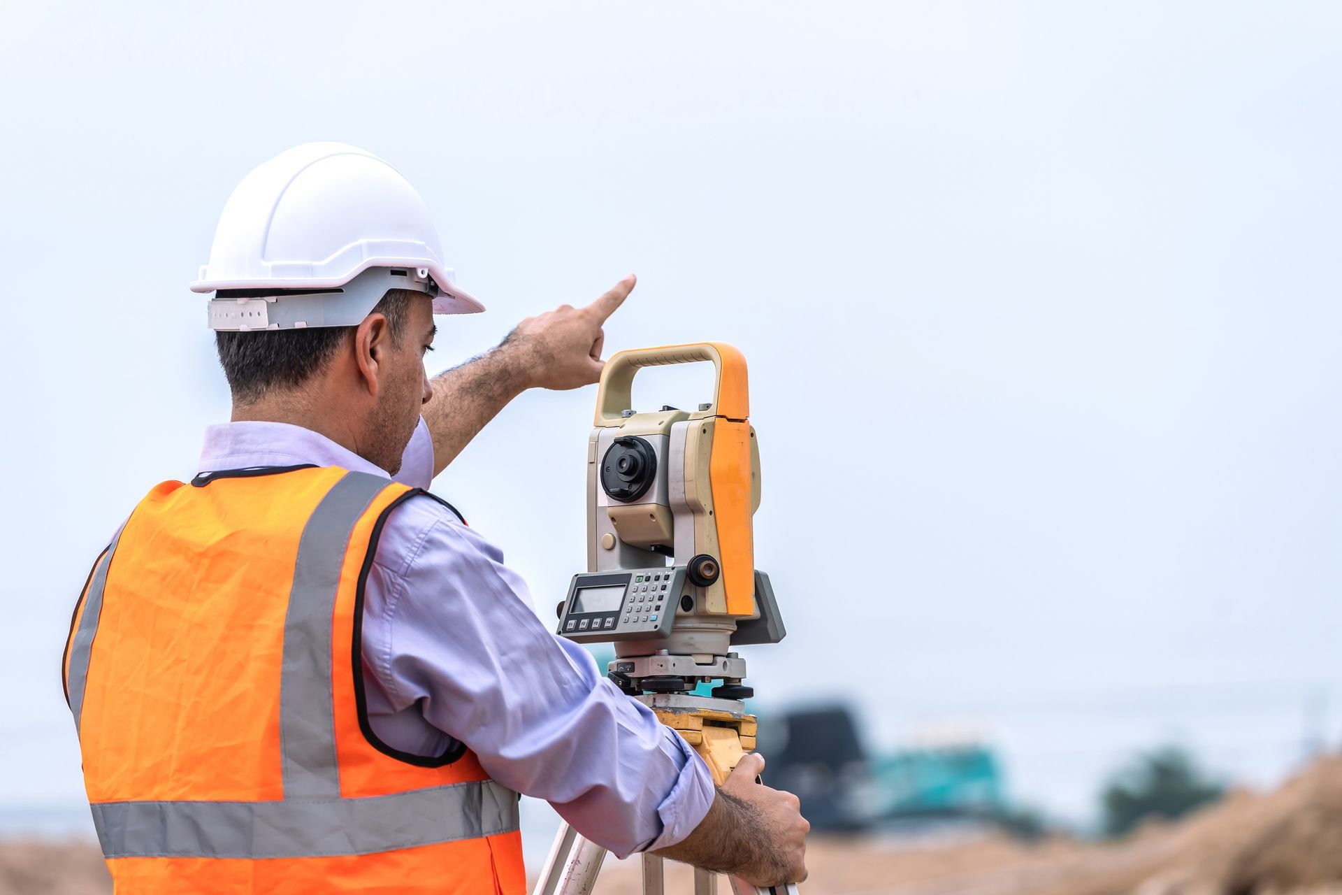 A construction worker is using a theodolite on a construction site.