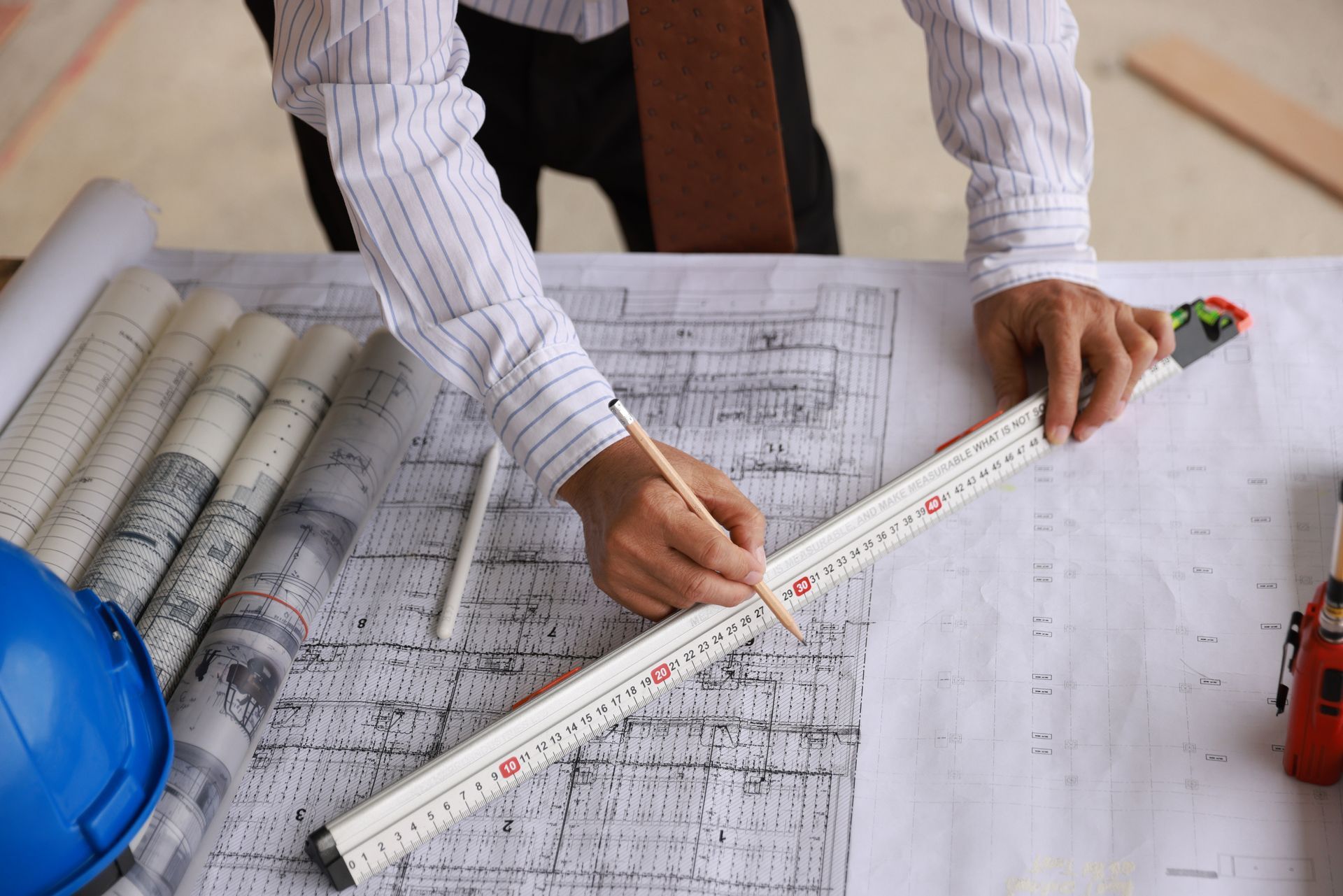 A man is measuring a blueprint with a tape measure.
