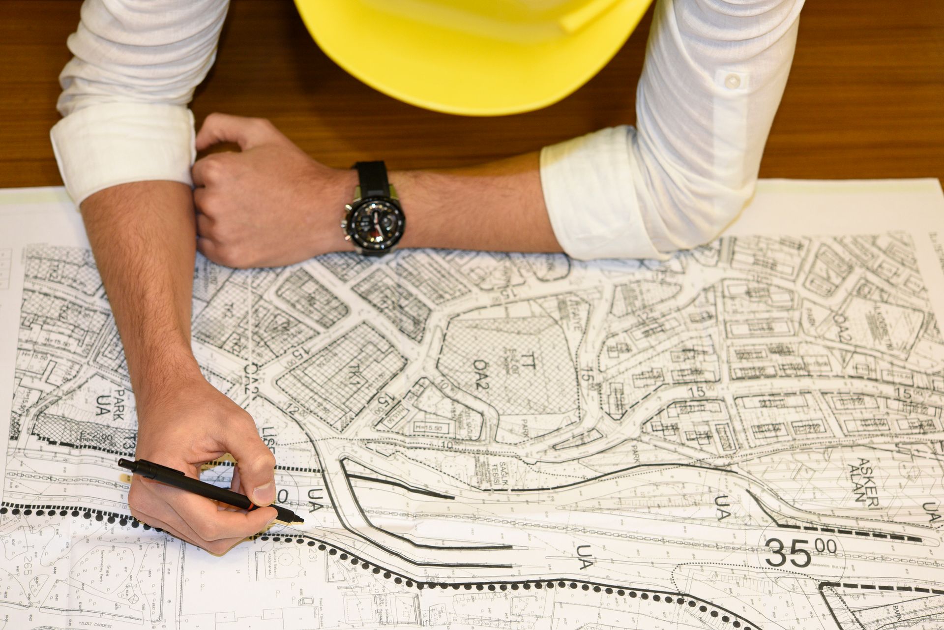 A person wearing a yellow hard hat is writing on a map.