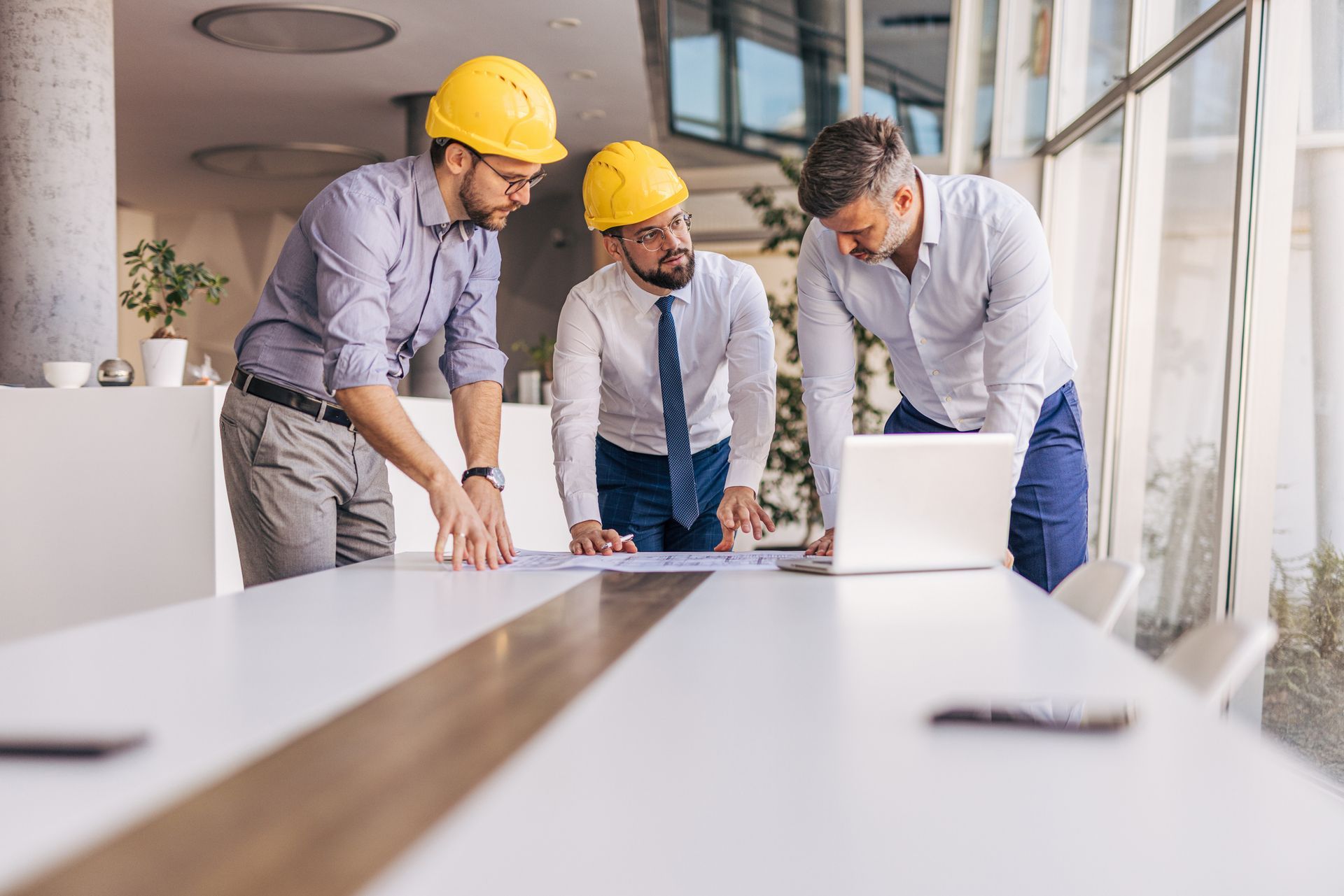 Three men wearing hard hats are looking at a laptop computer.