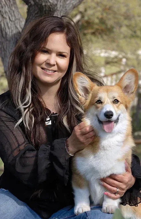 A woman is holding a corgi dog in her arms.