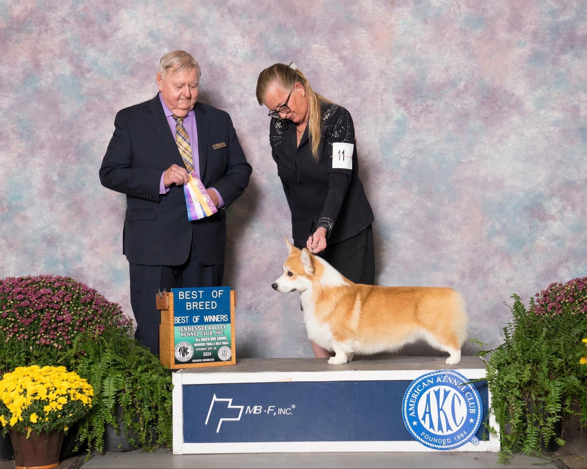 A man and a woman are standing next to a dog on a podium at a dog show.