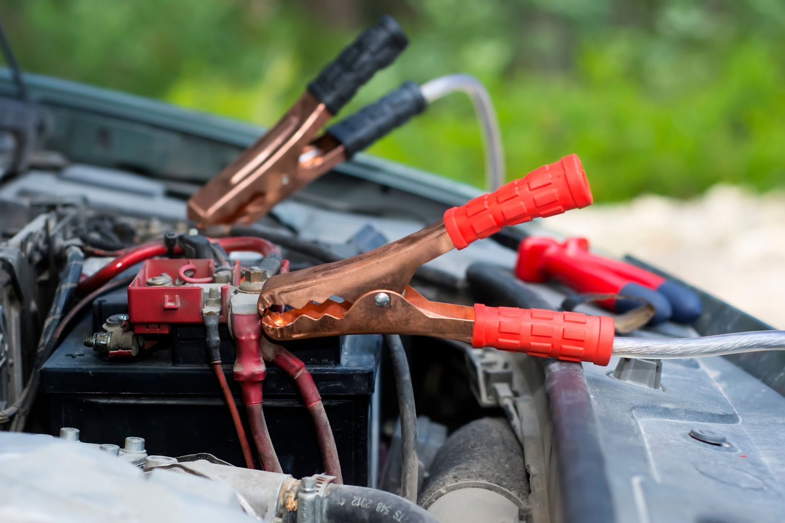 A close up of a car battery being charged with jumper cables.