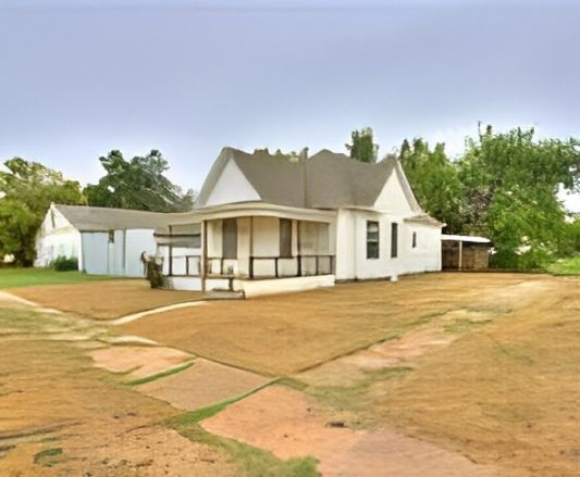 White house with porch, shed, and yard. Overcast sky.