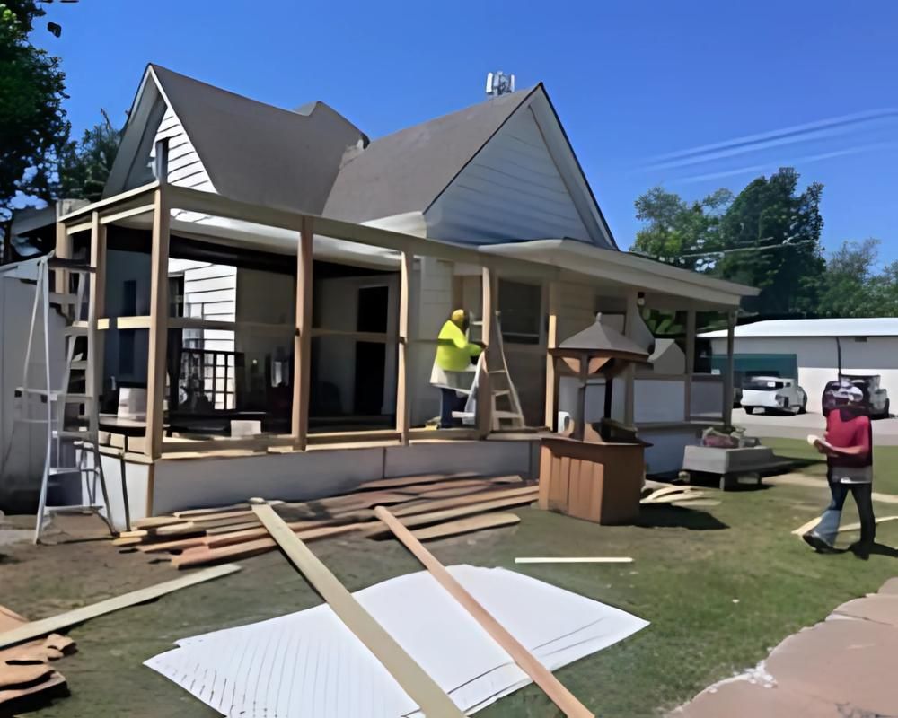 Construction workers building a wooden porch on a white house under a blue sky.