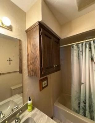 Bathroom with a dark wood cabinet above a bathtub. A sink and mirror are in view.