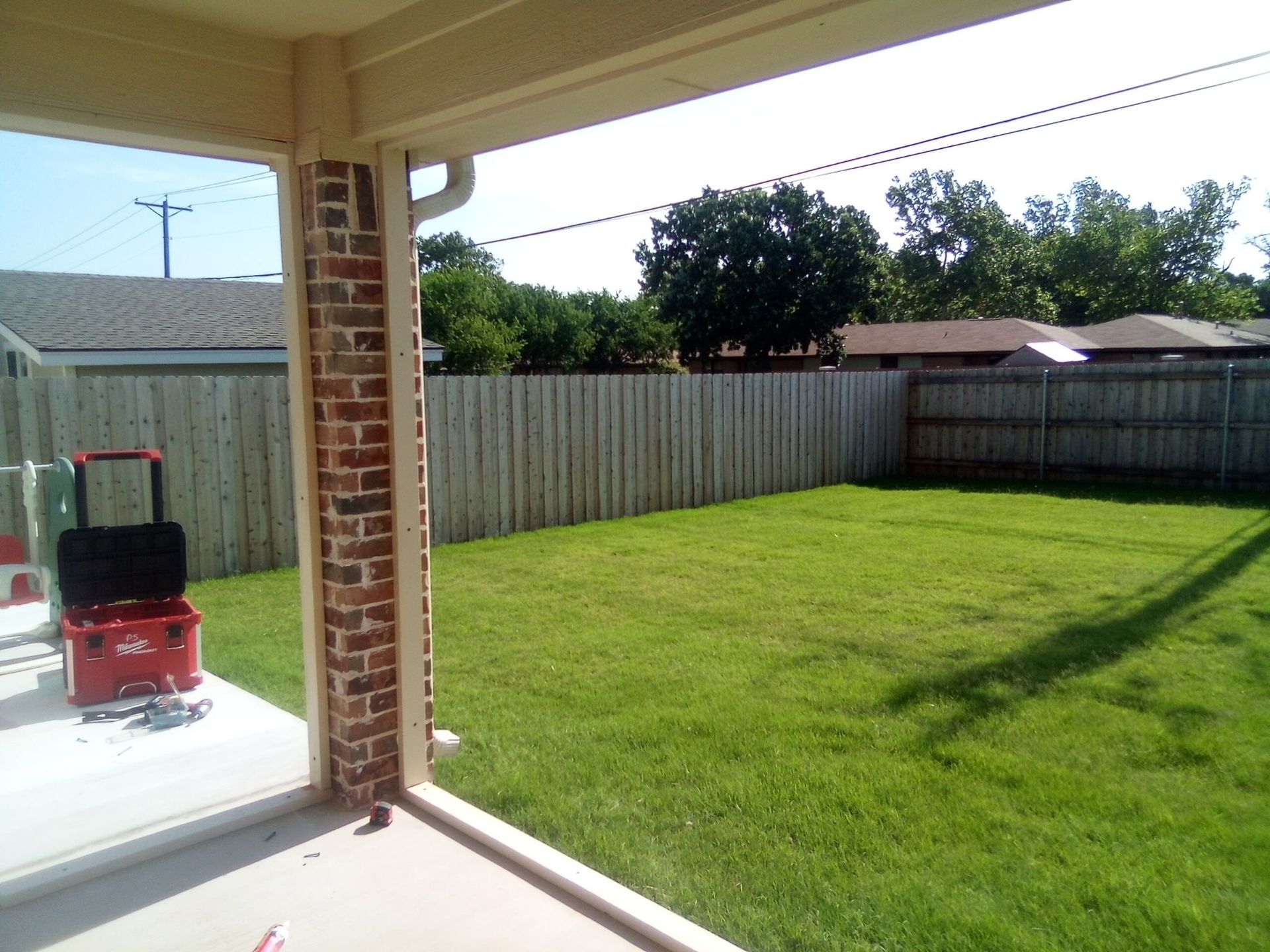 A brick-columned patio overlooks a grassy backyard with a wooden fence and trees.