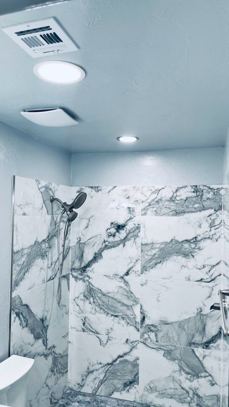 Bathroom with marble shower wall, overhead lighting, and showerhead.