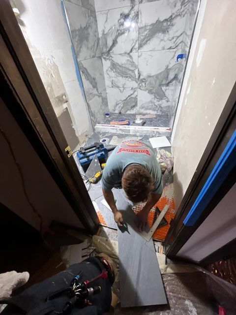 Person tiling a bathroom with marble-patterned tile, viewed from above.