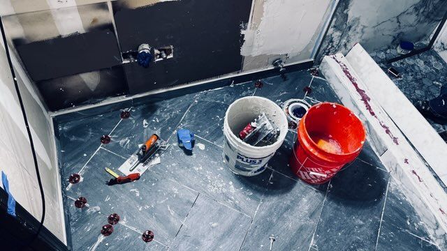 Bathroom under renovation with tools, buckets, and gray tiled floor and dark gray wall.