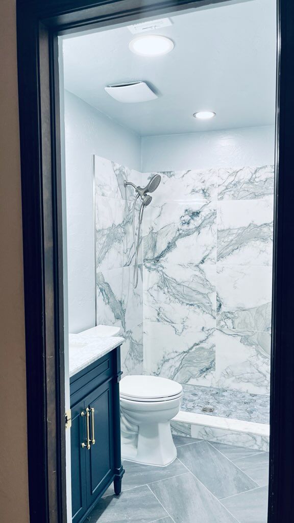 Bathroom interior with blue vanity, marble shower, and white toilet.