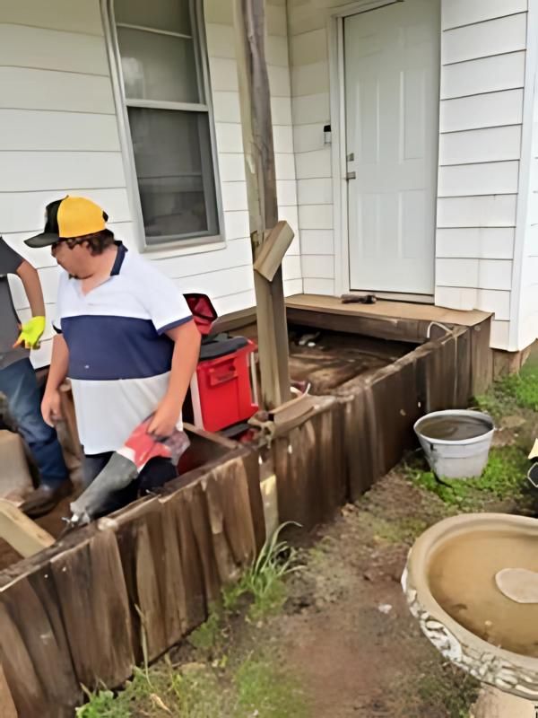 Man in white shirt, yellow hat, near wooden porch, red toolbox.
