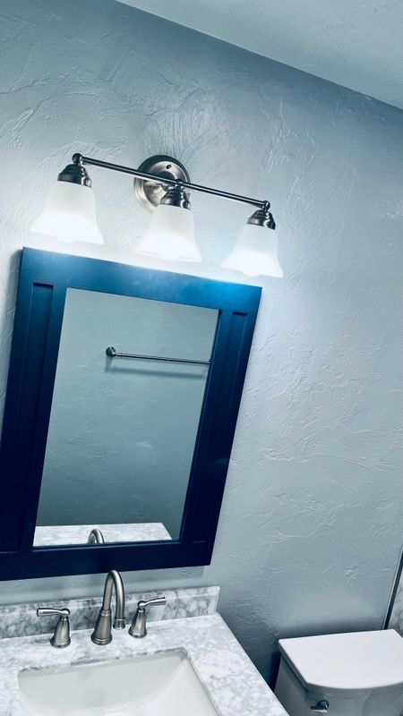 Bathroom vanity with blue-framed mirror, lit by a three-bulb fixture, white countertop and walls.