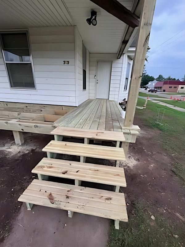 Newly constructed wooden steps and porch of a white house, with a door in the background, and dirt.